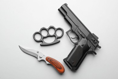 Black brass knuckles, gun and knife on white background, flat lay