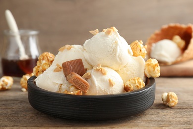 Plate of delicious ice cream with caramel candies and popcorn on wooden table, closeup