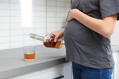 Future mother pouring alcohol drink from bottle into glass in kitchen, closeup. Bad habits during pregnancy