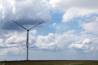 Modern wind turbine in field on cloudy day. Alternative energy source