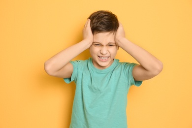 Little boy suffering from headache on color background
