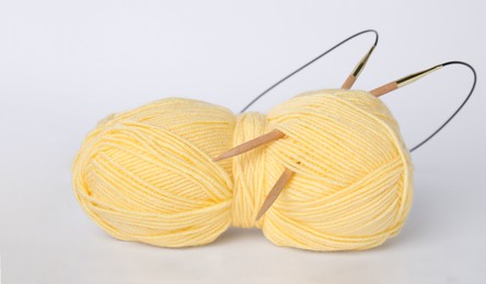 Soft woolen yarn and knitting needles on white background