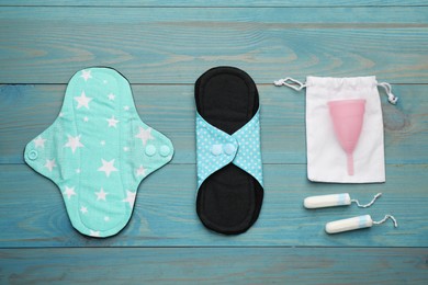 Reusable cloth pads, menstrual cup and disposable tampons on light blue wooden table, flat lay