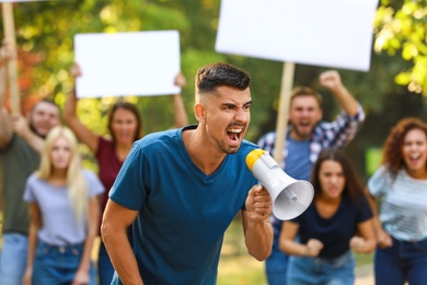 Photo of Angry young man with megaphone at protest outdoors
