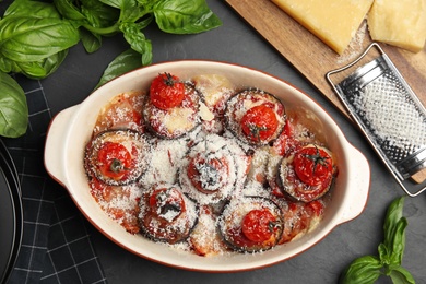 Baked eggplant with tomatoes and cheese served on black table, flat lay
