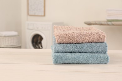 Stack of clean terry towels on white wooden table in laundry room