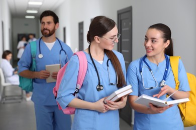 Smart medical students with books in college hallway, space for text