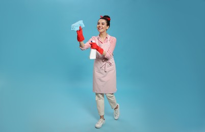 Young housewife with detergent and rug on light blue background