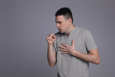 Young man coughing on grey background, space for text. Cold symptoms