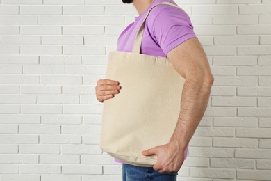 Man with cotton shopping eco bag against brick wall. Mockup for design