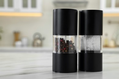 Salt and pepper mills on white marble table in kitchen. Space for text