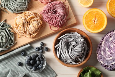 Photo of Rolled pasta painted with food colorings and ingredients on white wooden table, flat lay
