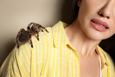 Photo of Scared young woman with tarantula on beige background, closeup. Arachnophobia (fear of spiders)
