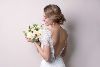 Young bride with elegant hairstyle holding wedding bouquet on beige background