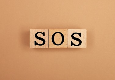 Abbreviation SOS made of wooden cubes on light brown background, top view