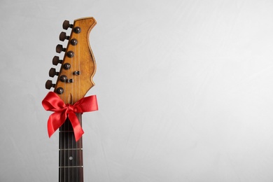 Guitar with red bow on light background, space for text. Christmas music