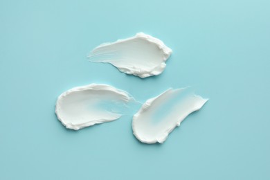 Samples of face cream on light blue background, top view