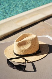Photo of Stylish straw hat and sunglasses on grey sunbed at poolside. Beach accessories