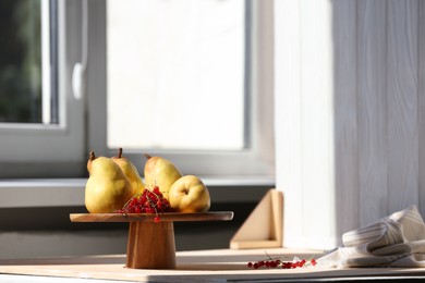 Stand with juicy pears, red currants and double-sided backdrop on table in photo studio. Space for text