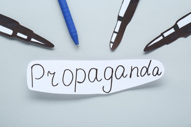 Photo of Information warfare concept, journalism and media influence. Pen and paper bullets aimed at card with word Propaganda on white background, flat lay