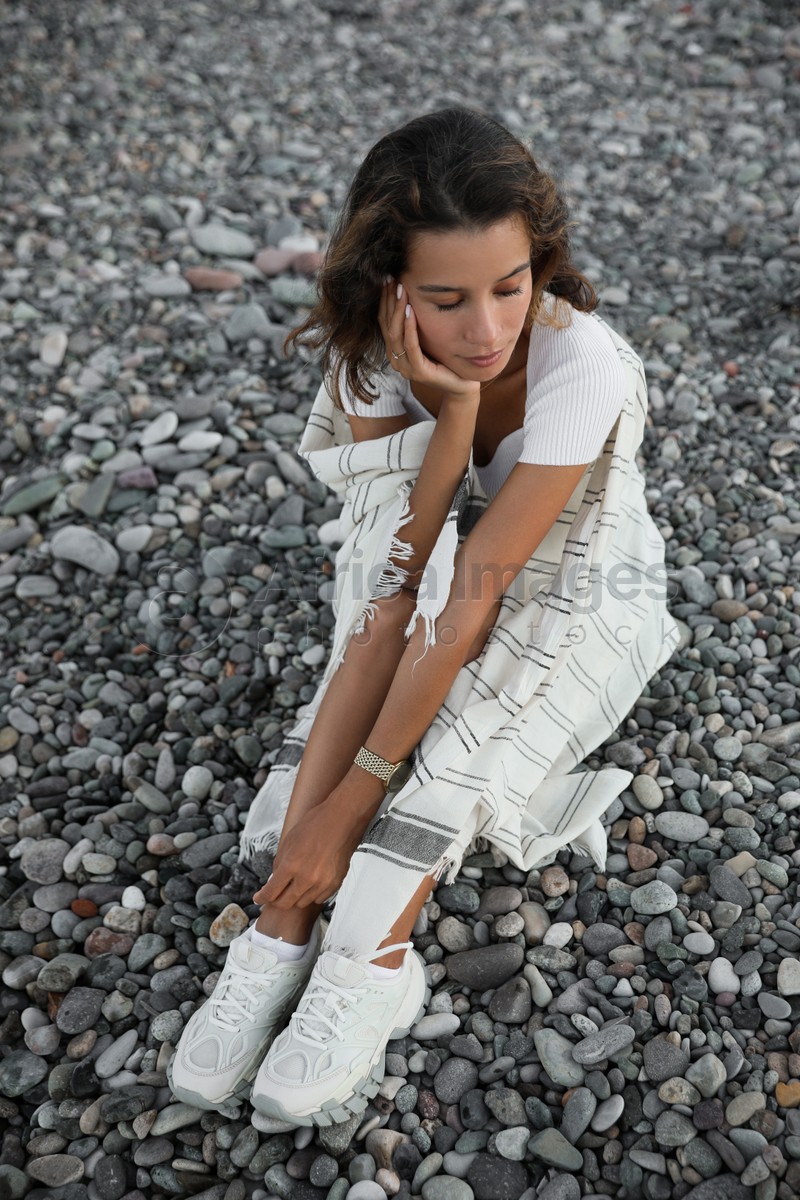 Beautiful young woman sitting on pebble beach