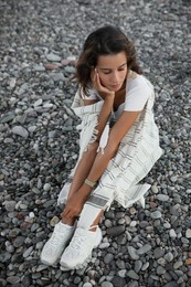 Beautiful young woman sitting on pebble beach