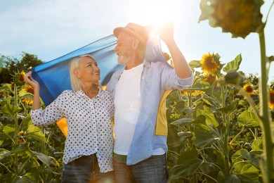 Happy mature couple with national flag of Ukraine in sunflower field