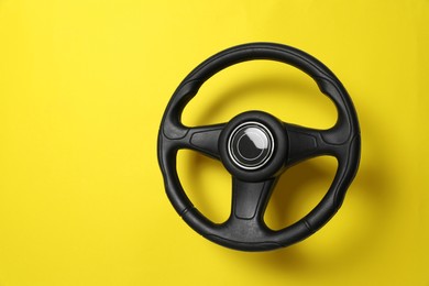 New black steering wheel on yellow background, space for text