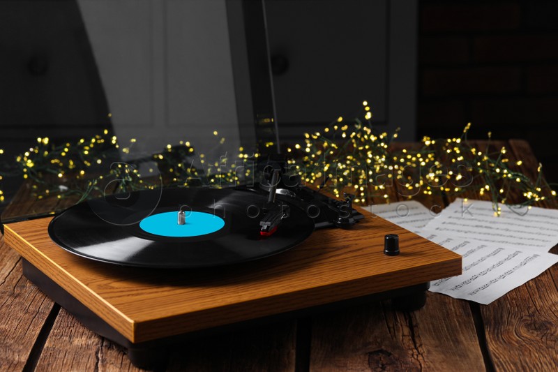 Photo of Turntable with vinyl record, note sheets and fairy lights on wooden table