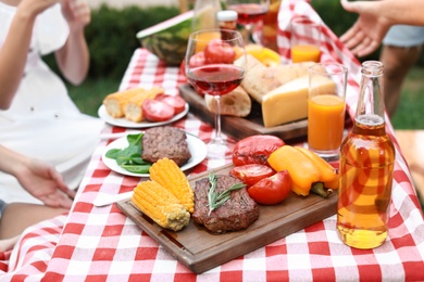 Photo of Friends at barbecue party, focus on table with cooked meat and vegetables outdoors