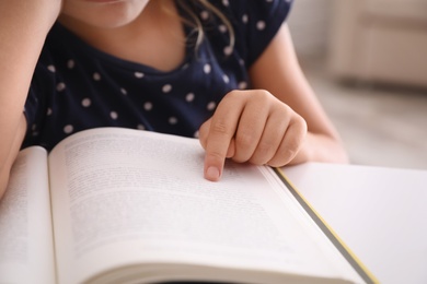 Cute little girl with book doing homework at table, closeup