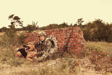 Image of Man in military uniform with German shepherd dog near broken brick wall