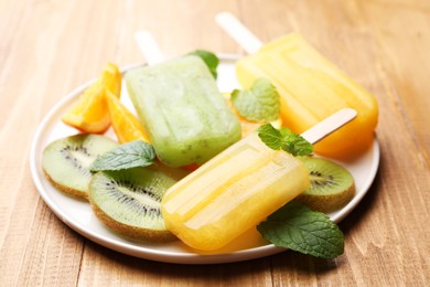 Plate of tasty orange and kiwi ice pops on wooden table. Fruit popsicle