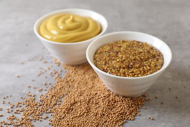 Photo of Bowls with mustard and seeds on grey table, closeup