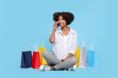 Photo of Happy African American woman with shopping bags talking on smartphone against light blue background