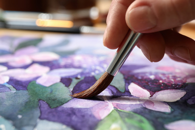 Woman painting beautiful flowers with watercolor, closeup