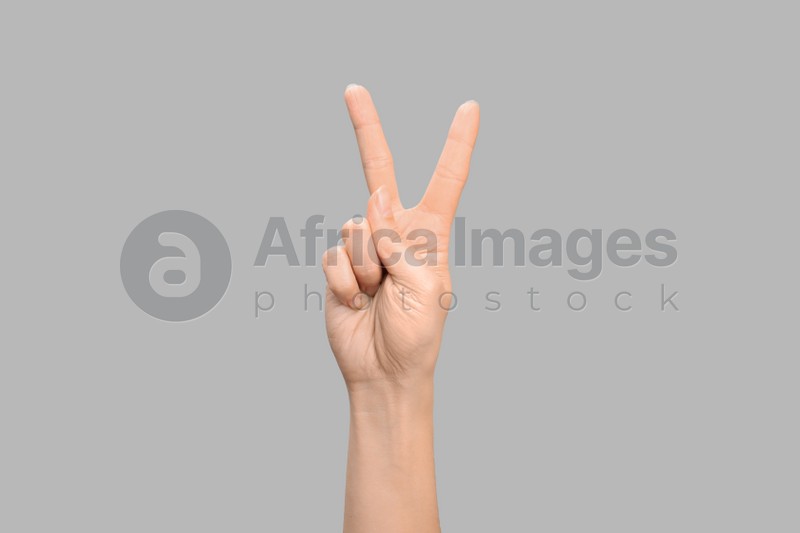 Photo of Woman showing V letter on grey background, closeup. Sign language