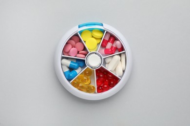 Plastic box with different pills on light grey background, top view