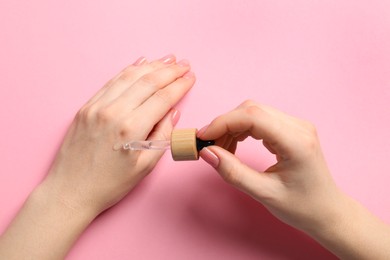 Woman dripping serum from pipette on her hand against pink background, closeup