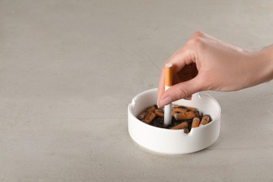 Woman putting out cigarette in ashtray on grey table, closeup. Space for text