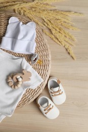Baby bodysuit, hat, booties, toy and spikelets on wooden background, flat lay