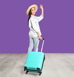 Beautiful woman with suitcase for summer trip near purple wall. Vacation travel