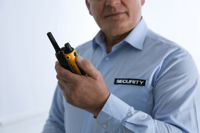 Professional security guard with portable radio set on light background, closeup