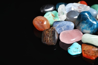 Photo of Different beautiful gemstones on black background, closeup. Space for text