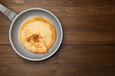 Frying pan with delicious crepes on wooden table, top view. Space for text