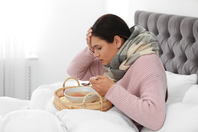 Sick young woman eating soup to cure flu in bed at home