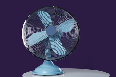 Modern electric fan on white table against violet background