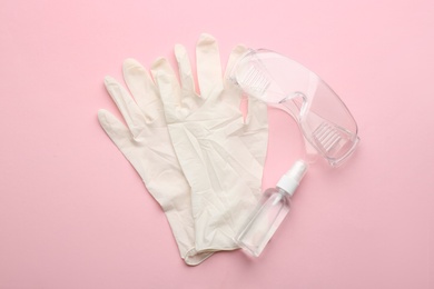 Medical gloves, goggles and hand sanitizer on pink background, flat lay