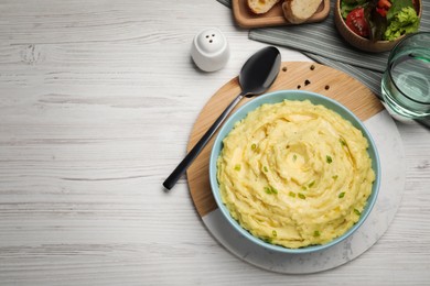 Photo of Bowl of tasty mashed potatoes with greens served on white wooden table, flat lay. Space for text