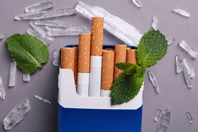 Pack of cigarettes, menthol crystals and mint leaves on grey background, flat lay
